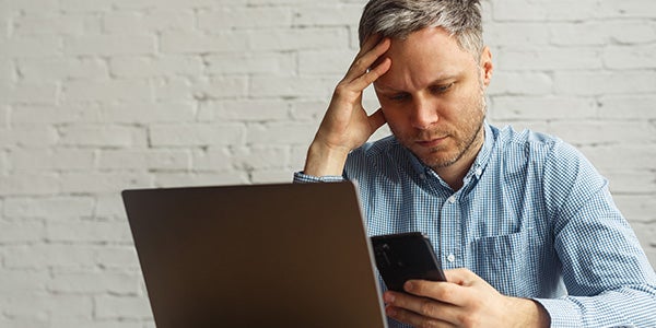 Stressed out man viewing phone and laptop